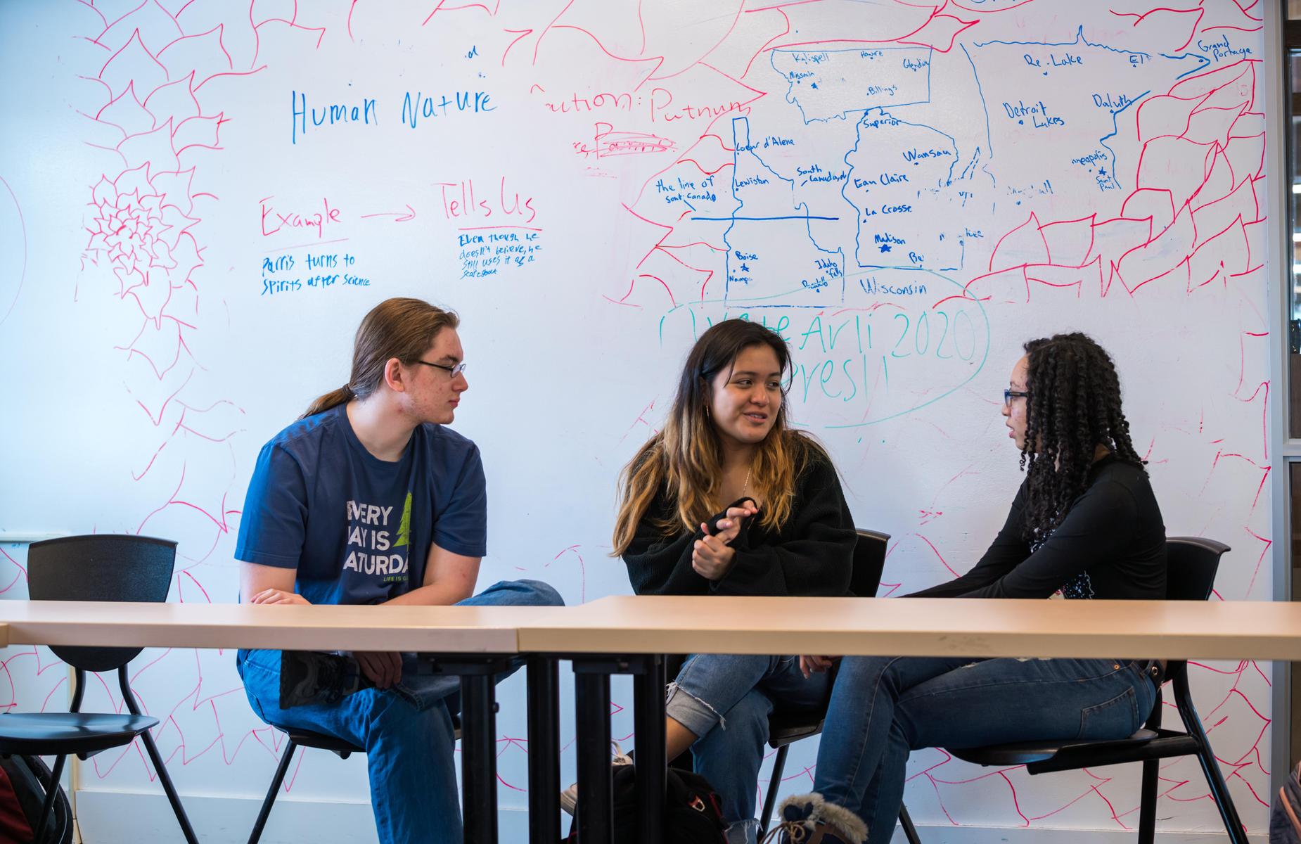 Three students having a discussion in a classroom.