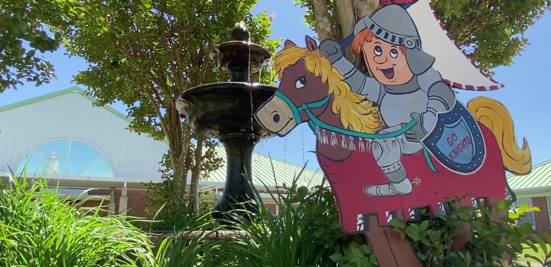 Fountain with a cartoon knight riding a horse in front of a school building.