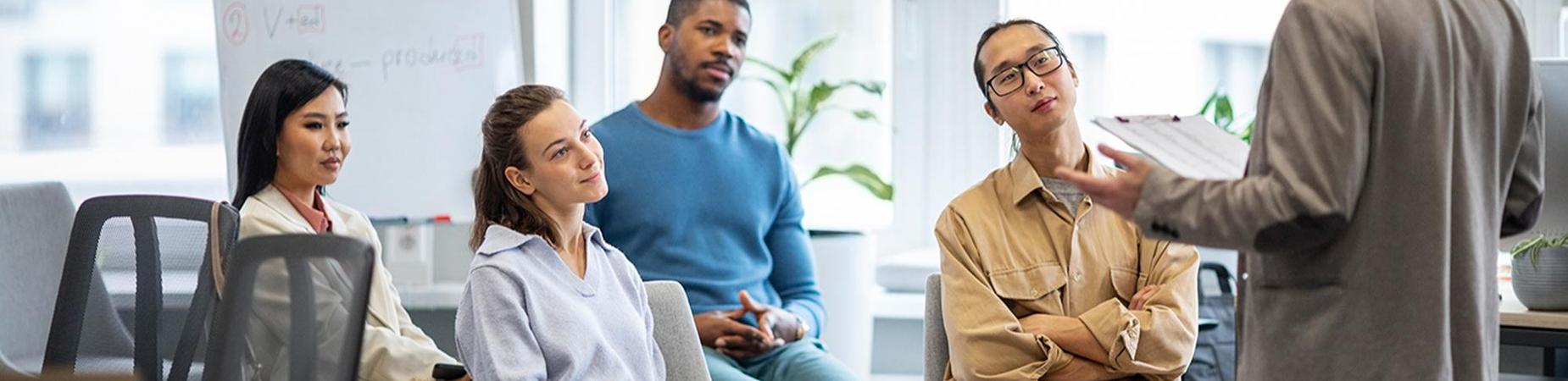 A man standing and talking to a diverse class of adults.