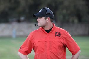Referee in an orange shirt and cap watching a sports event.