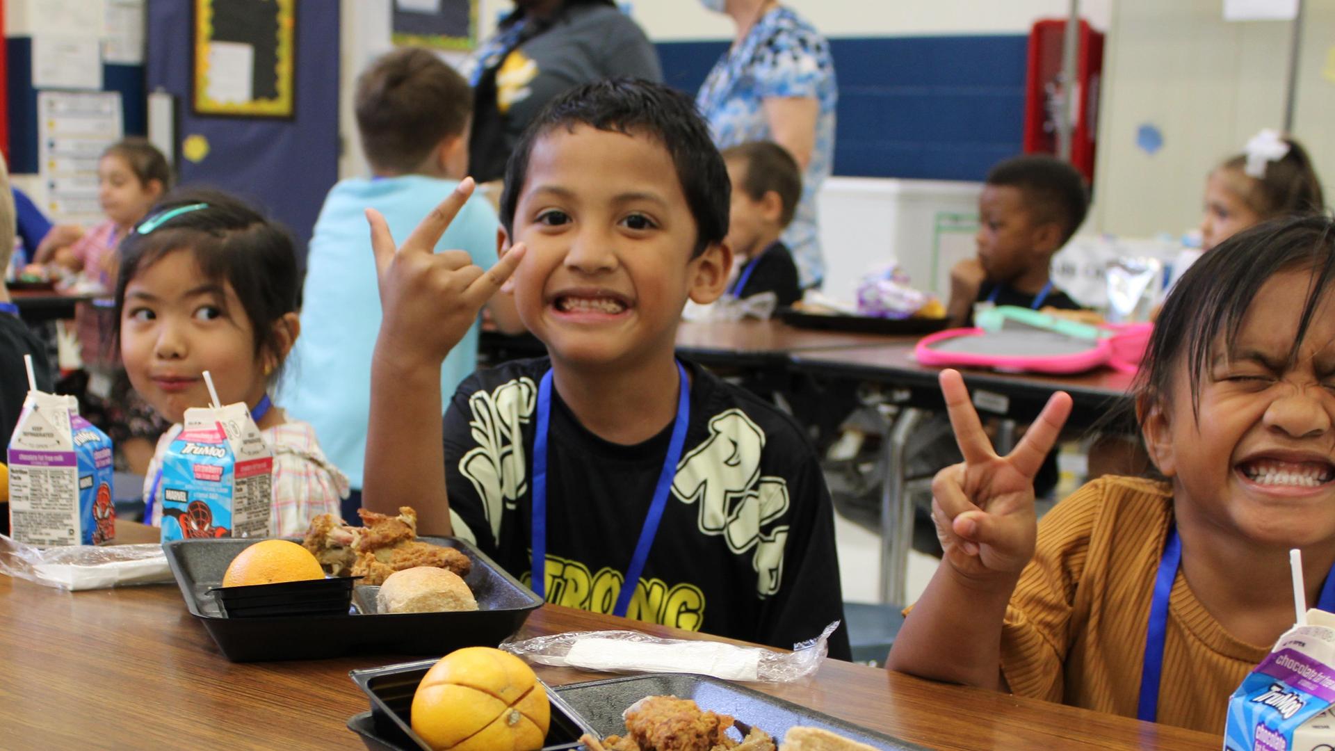 Children enjoying lunch with smiles and playful gestures in a classroom.