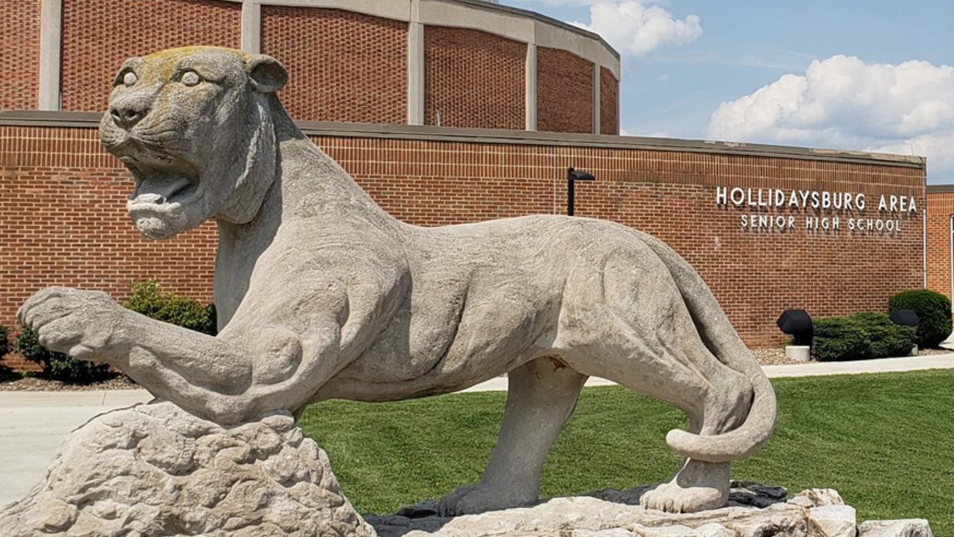 A stone statue of a lioness in front of a school building.