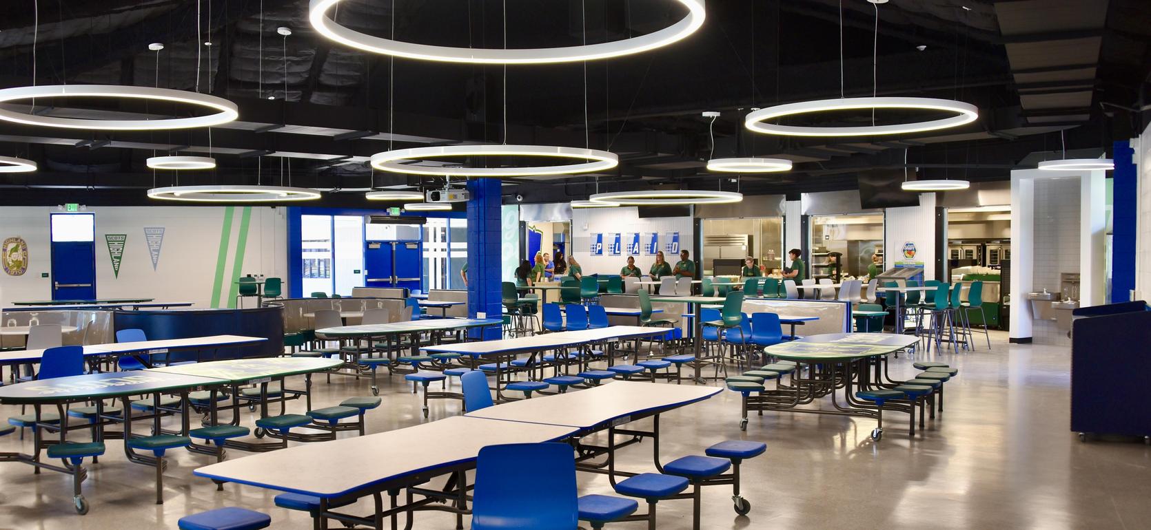 Bright cafeteria with circular lights and rows of tables and chairs.