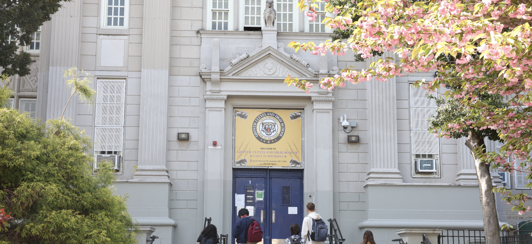 Students walking toward a large school entrance with a decorative banner.