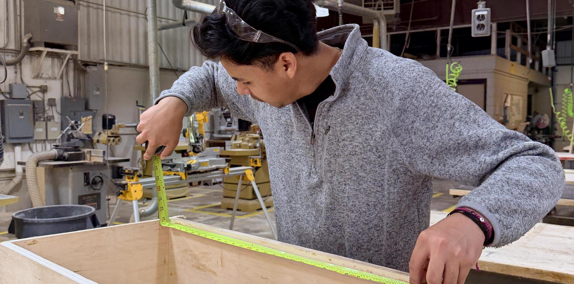 A person measuring wood with a measuring tape in a workshop.