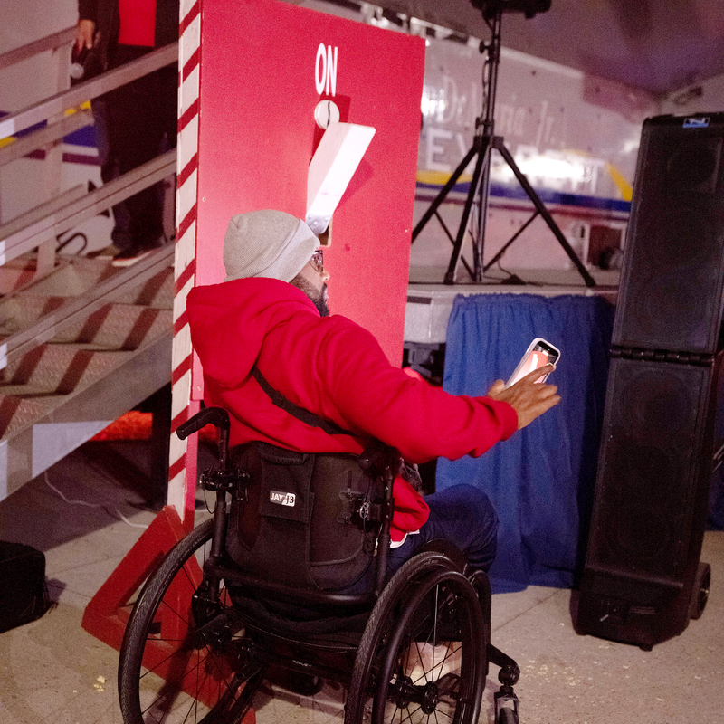 Person in a wheelchair wearing a red hoodie, interacting with a smartphone near a large sign.