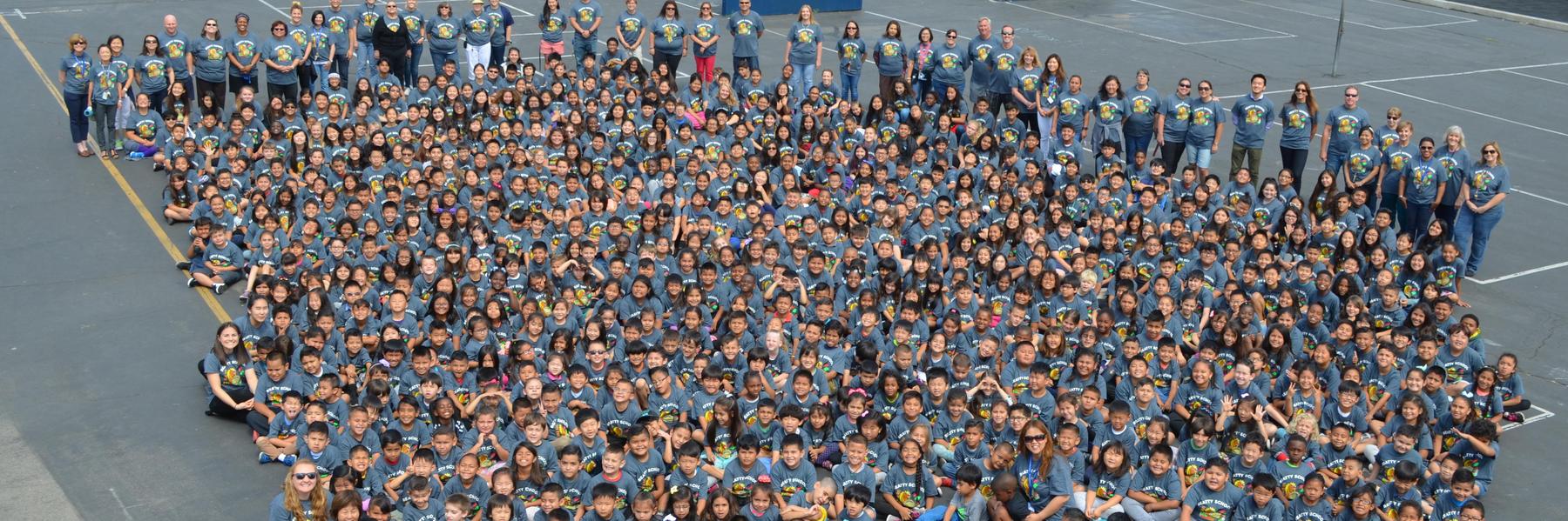 Students and staff gather together on the playground for an aerial view photo opportunity in their 2017-18 reading t-shirts.