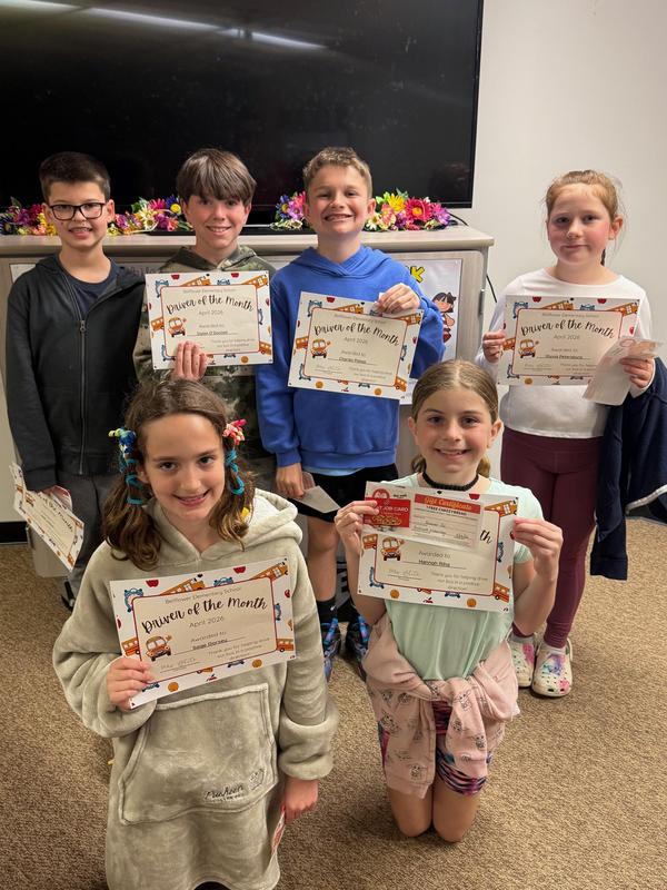 Six children posing with 'Driver of the Month' certificates in a classroom.