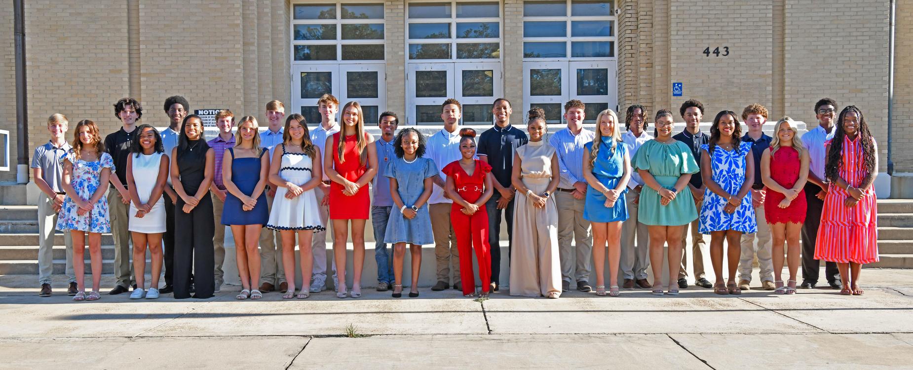 A diverse group of people posing together in front of a school building.