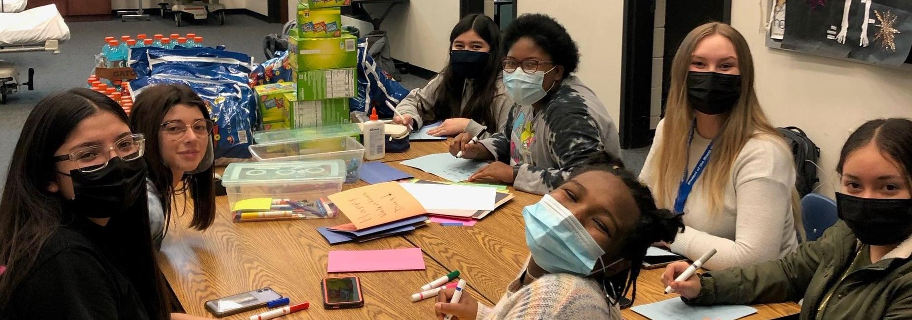 7 girls around a table with markers and paper
