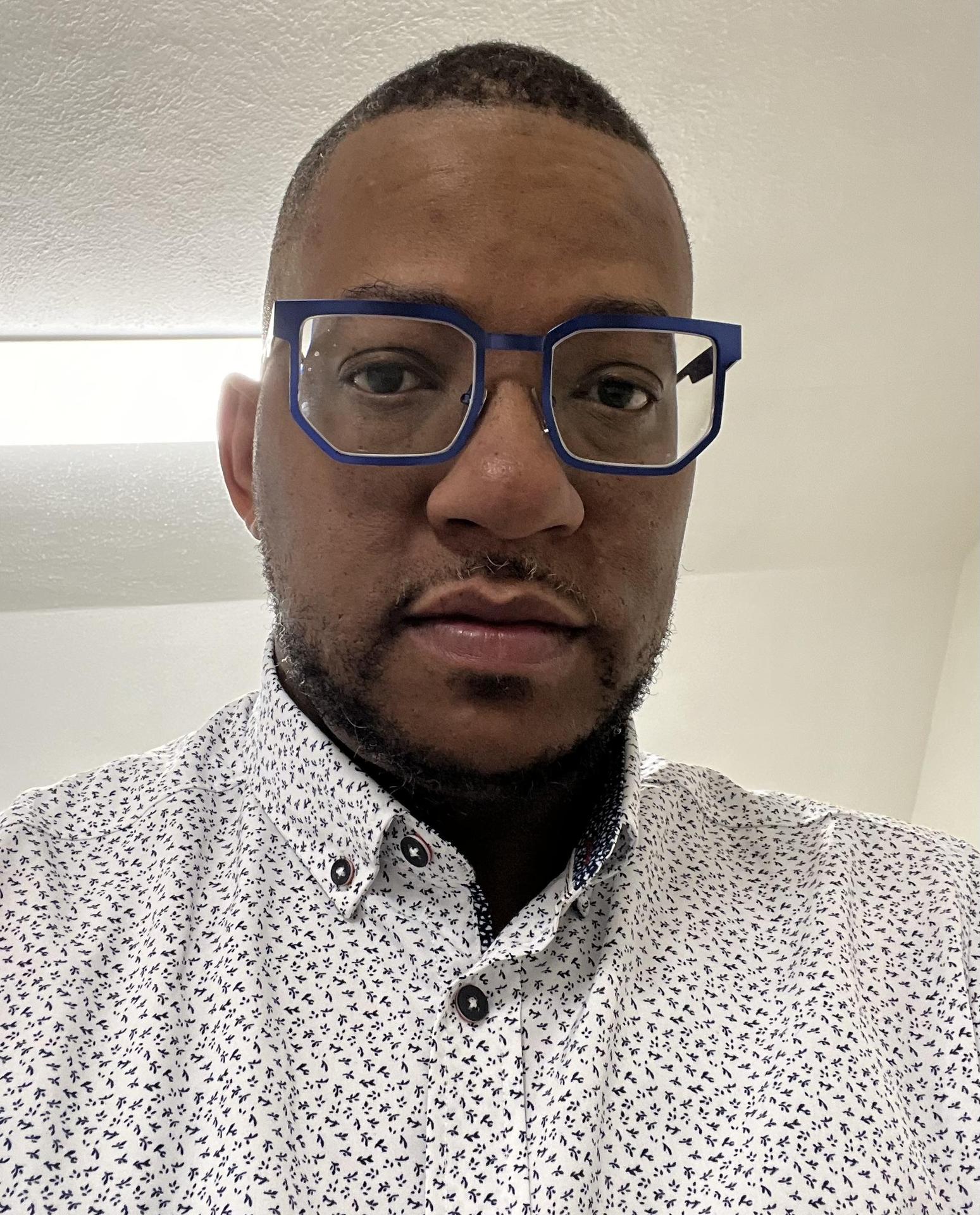 Black man with blue glasses in a white collared shirt
