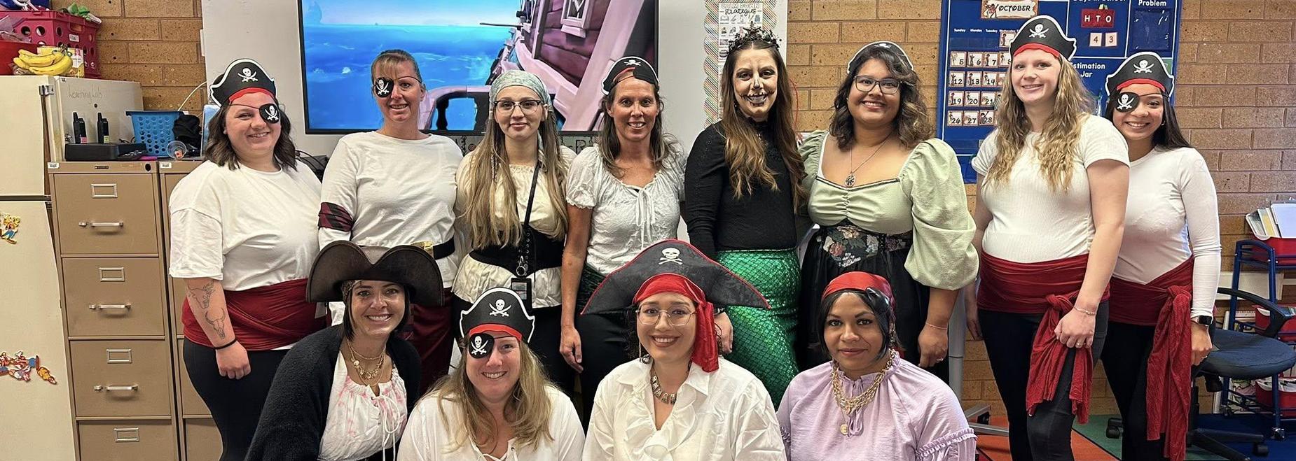 A group of people dressed as pirates, posing together in a classroom setting.