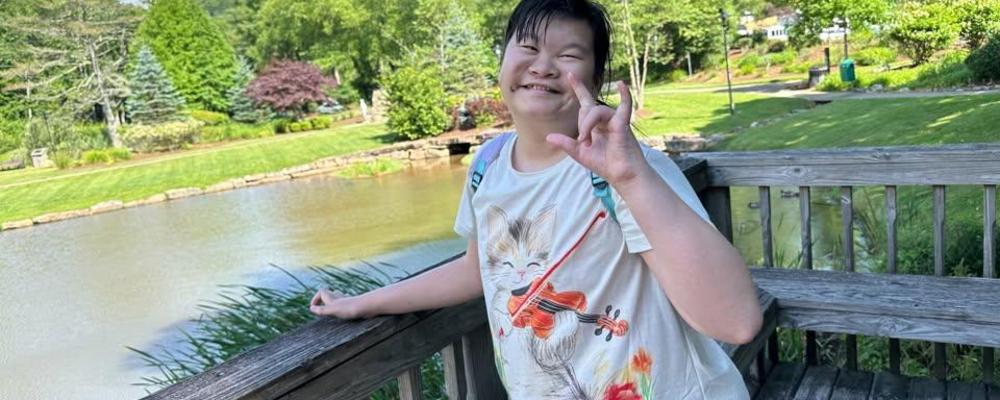 A girl smiling and posing by a pond in a park.