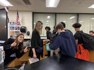 A group of students receiving items from a smiling classmate in a lab environment.