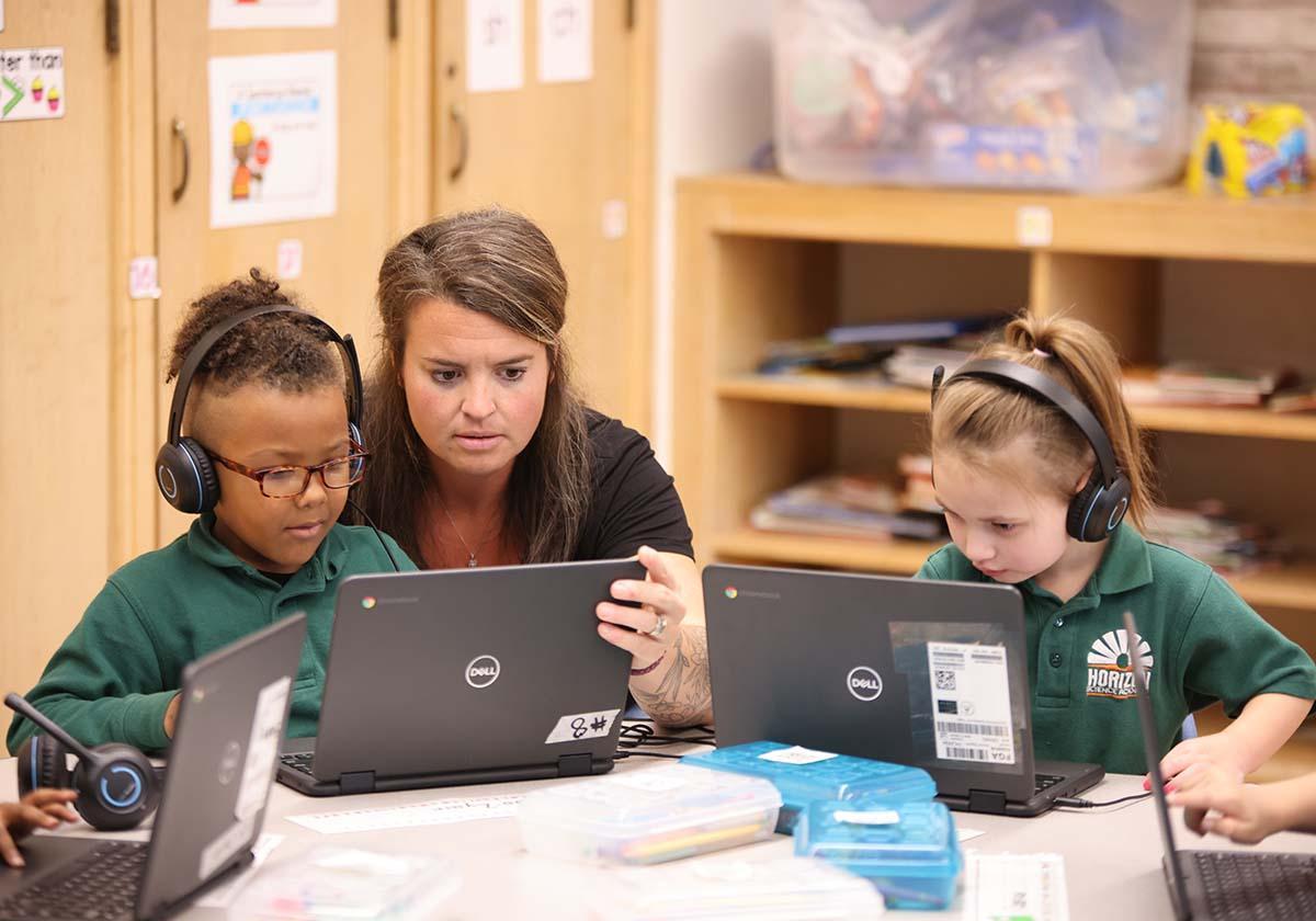 HSA Teacher smiles while kneeling beside a young student in a classroom setting.