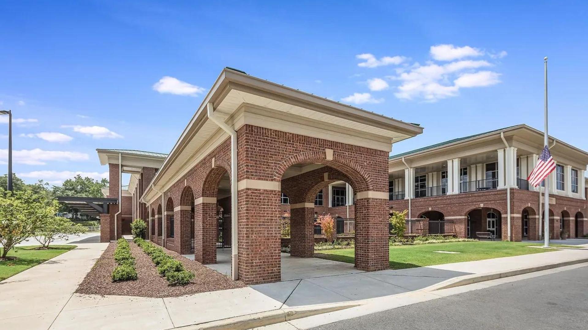 Brick building with arches, landscaped area, and an American flag.