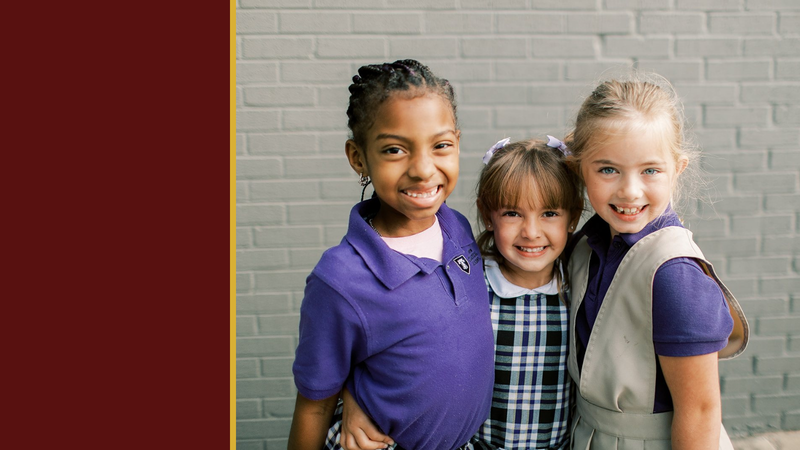 Three smiling young students stand together by a brick wall