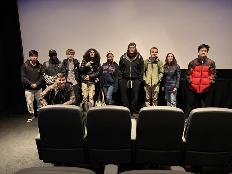 Group of young people gathered in a cinema, seated in front of empty chairs.