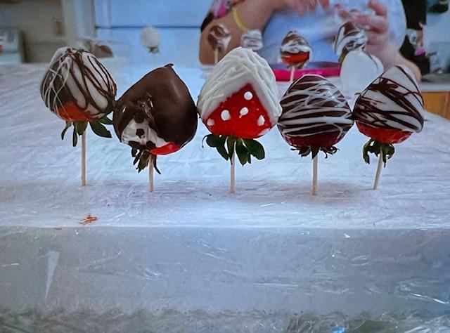 Five decorated chocolate-covered strawberries on sticks.