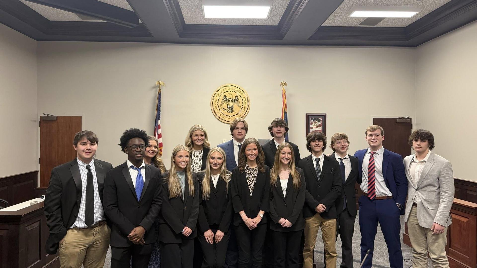 A group of students in formal attire posing in a courtroom setting.