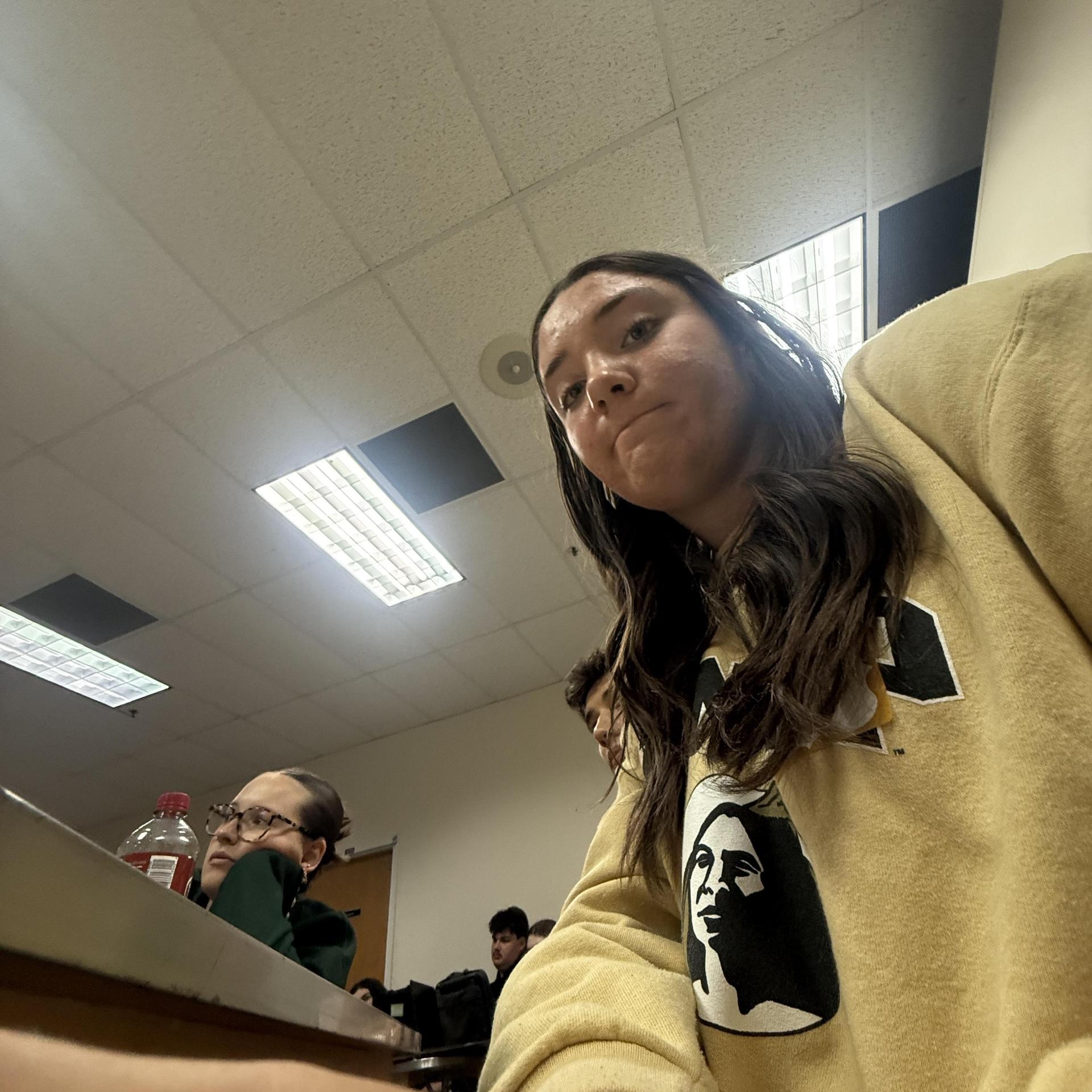 Student sitting at a table with classmates in a classroom setting.