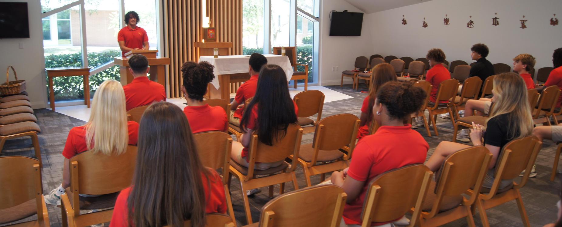 1 male student leads prayer at podium in chapel