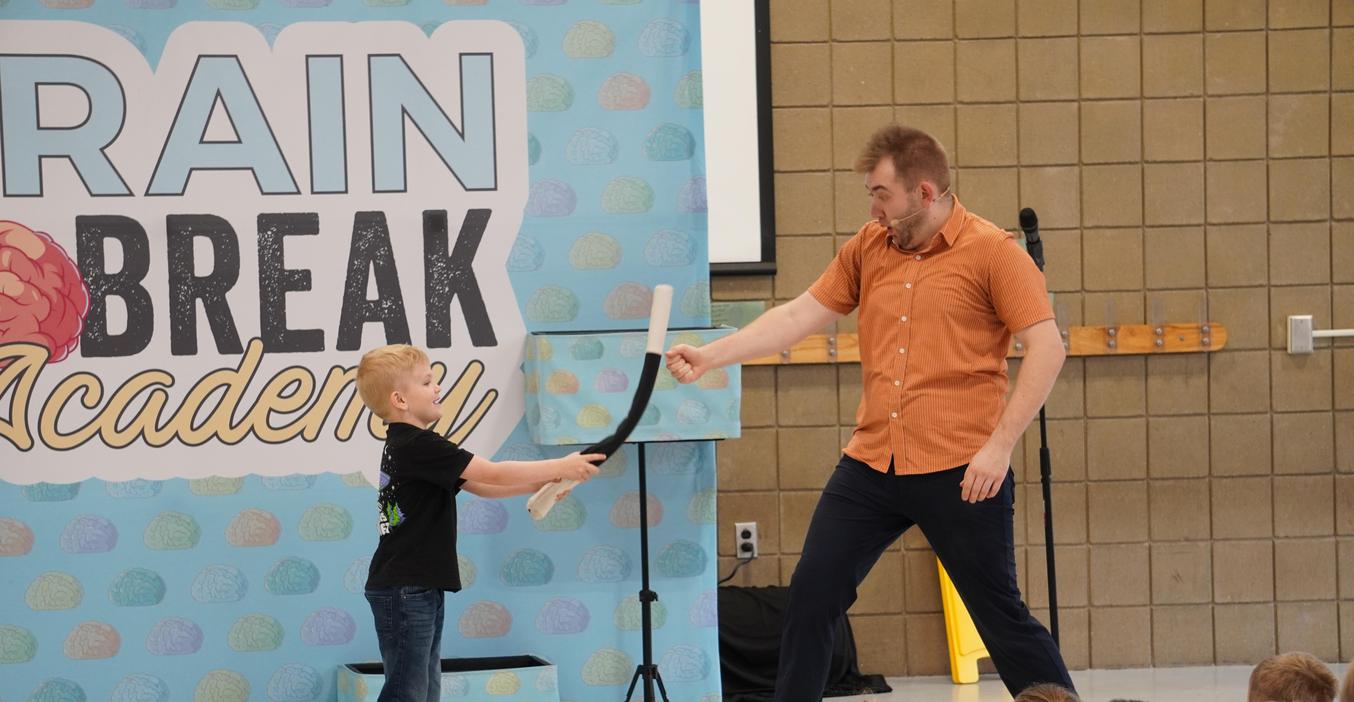 A student taps a magician's hand with a magic wand.