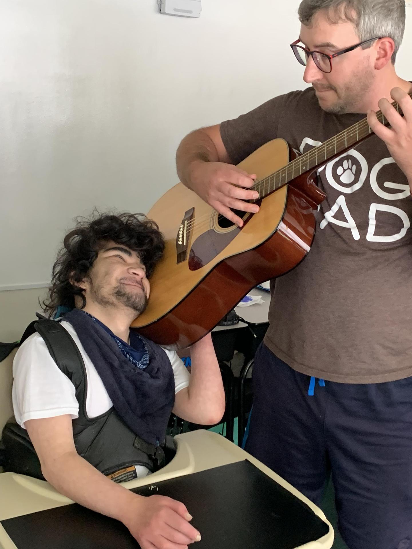  Staff playing guitar; student smiling, hugging guitar to face