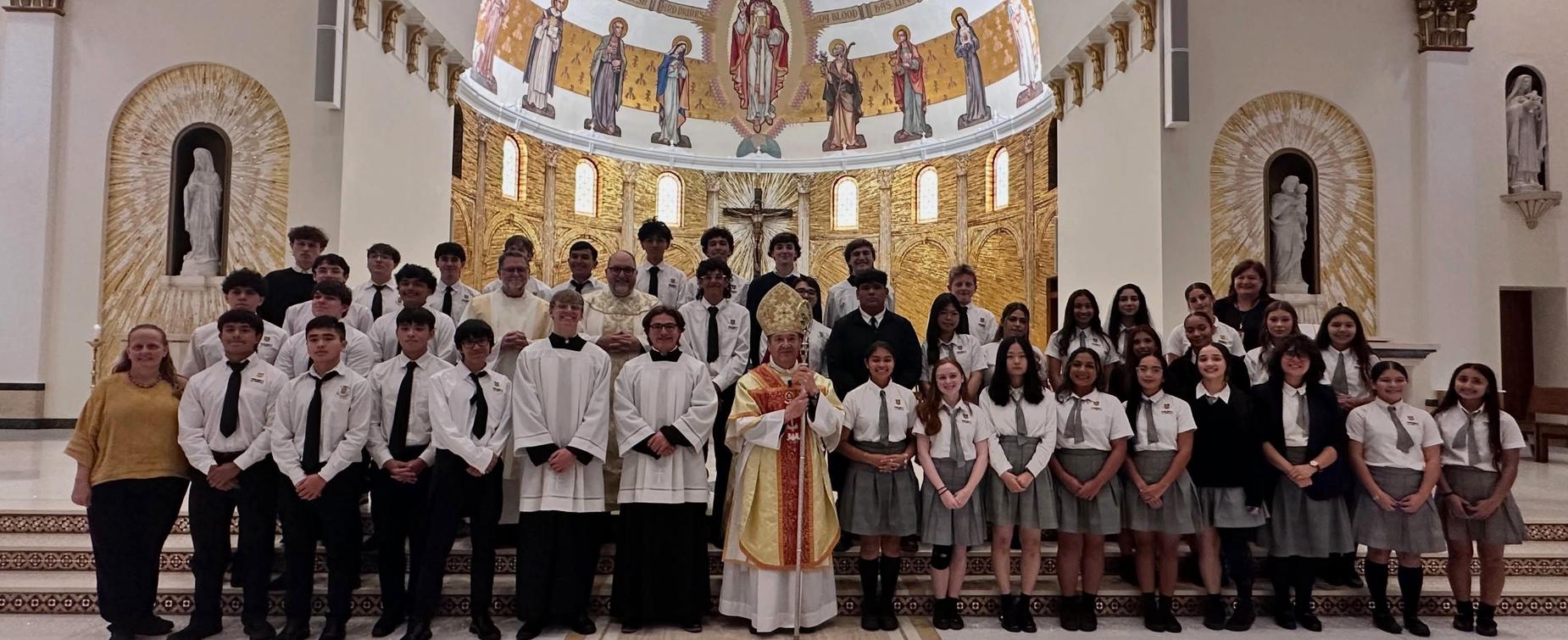 A large group of people in formal attire posed inside a brightly decorated church.