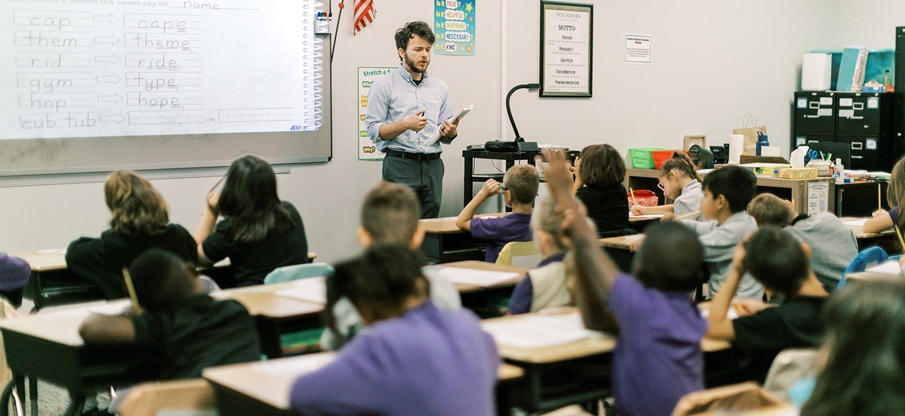 A teacher leads a lesson as students raise their hands