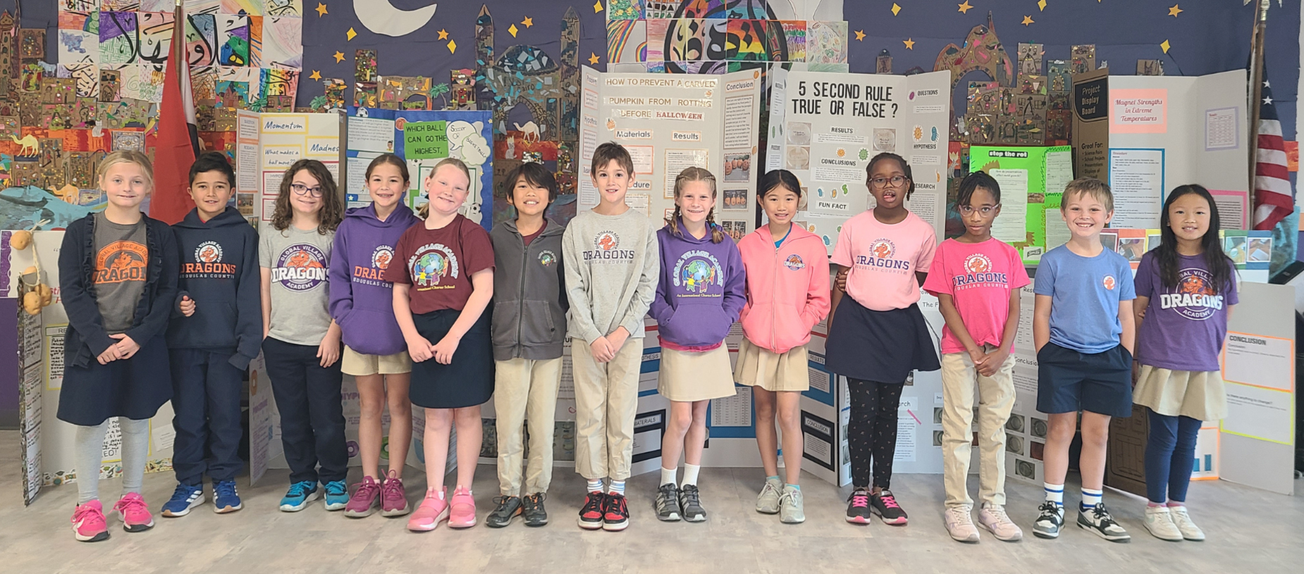 A diverse group of students standing together in a classroom with colorful displays behind them.