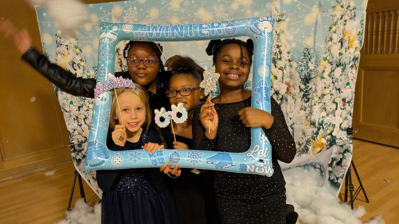 Four girls pose with a picture frame in front of a snowy backdrop