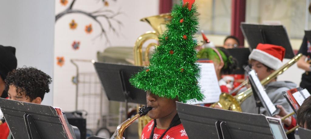 boy plays the saxophone while wearing a glittering Christmas tree hat