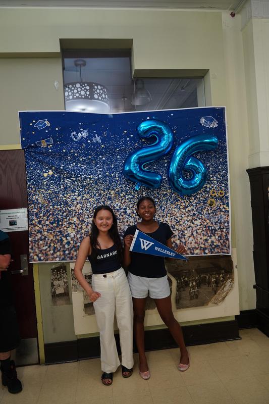 Two girls posing by a festive backdrop with balloons and decorations.
