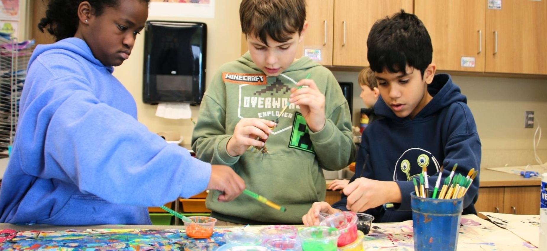 Three kids engage in an arts and crafts activity, using paint and materials at a table.