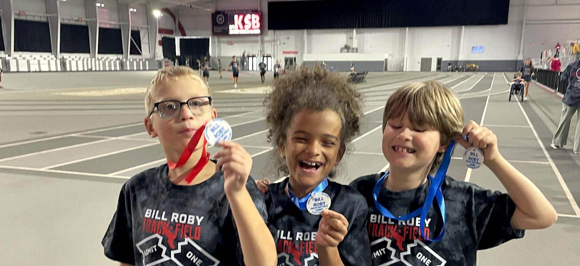 Three children smiling and holding medals at a sports event.
