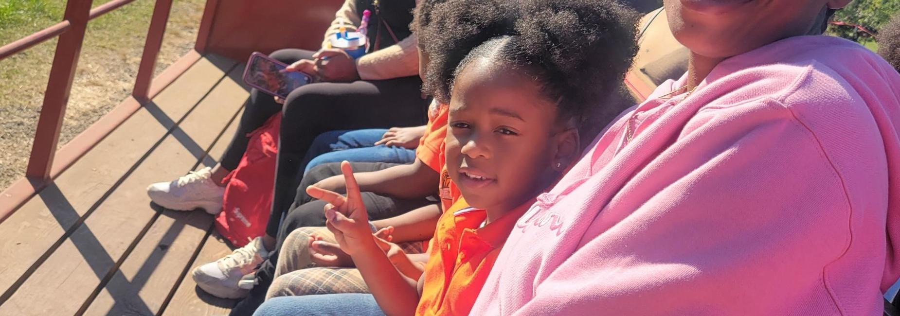 Students and family members enjoy a field trip to a farm. Students are smiling back at the camera with their parents enjoying the sunshine and learning about animals.