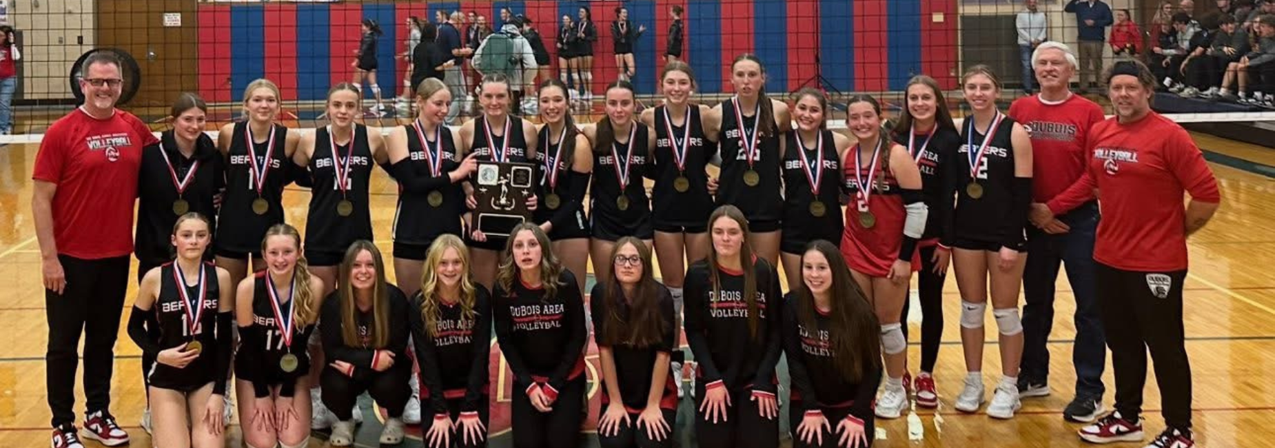 Group photo of the victorious volleyball team holding medals and a trophy in a gym.