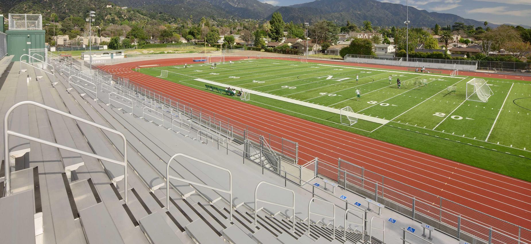 A view of a sports field with bleachers, track, and distant mountains.