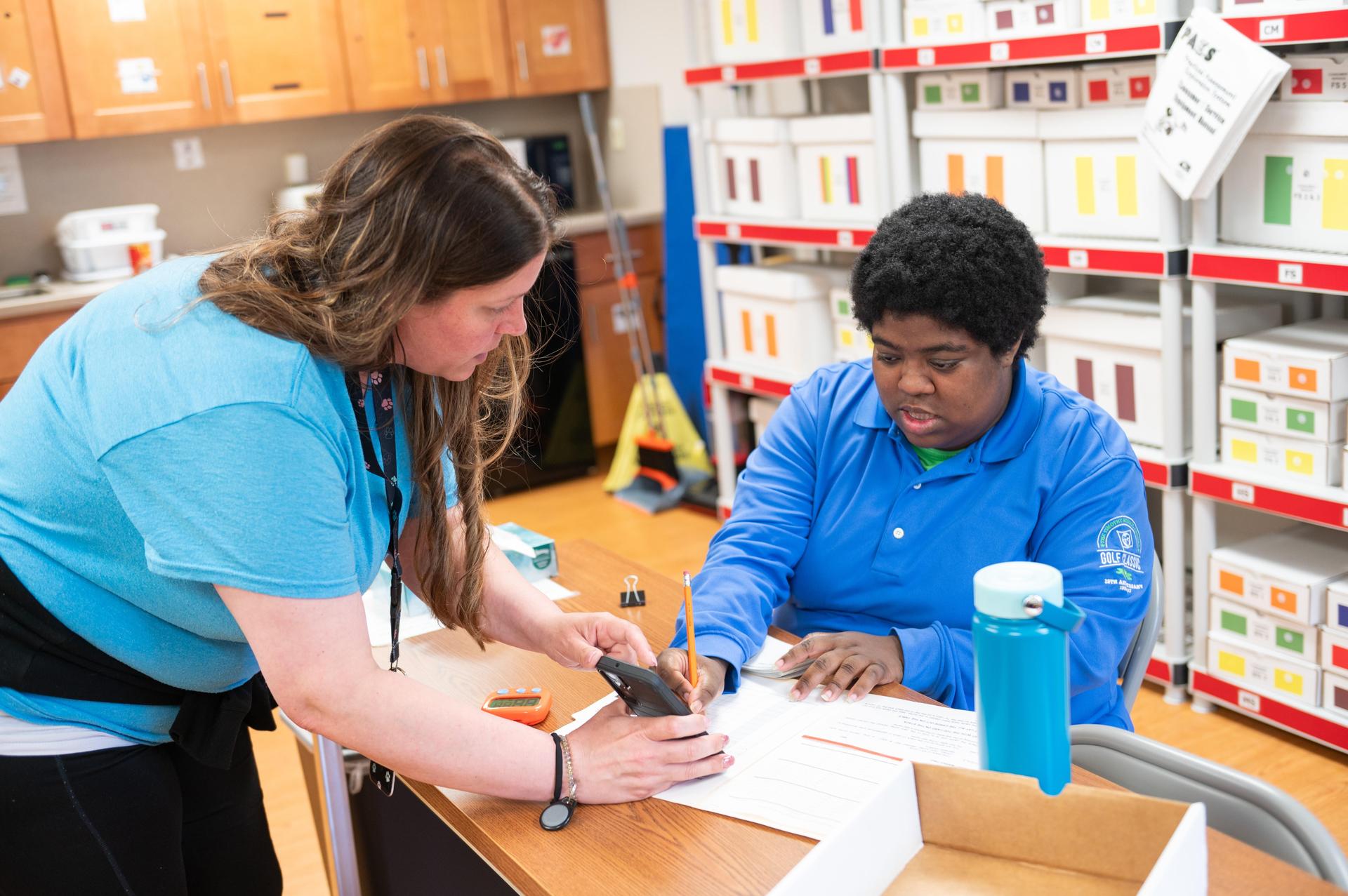 Teacher and student both wearing blue shirts at desk.