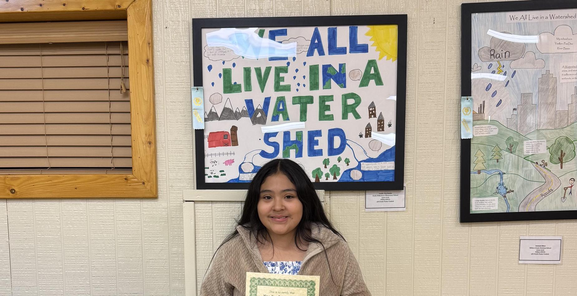 Child holding an award certificate in front of a colorful poster on the wall.