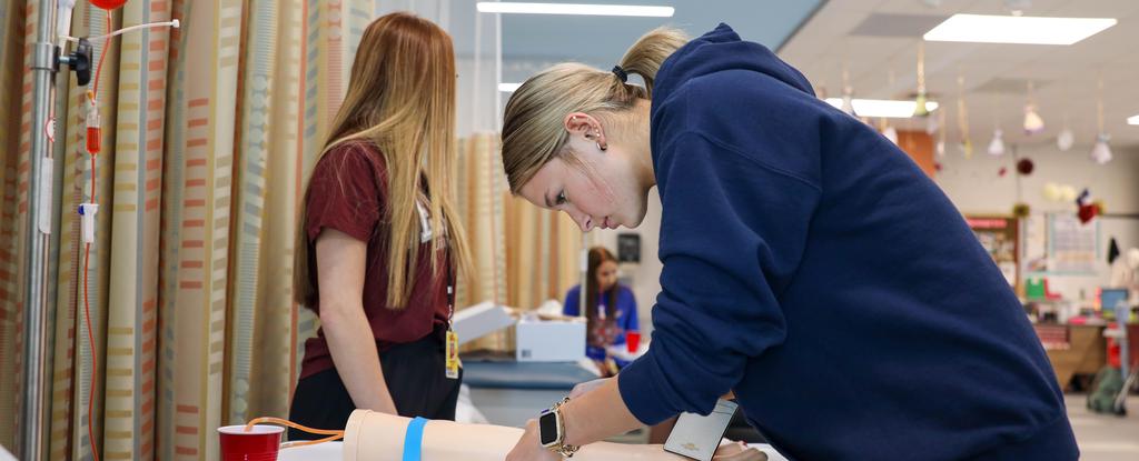 Two CTE students working on a project in a classroom, one observing and one focused on their task.