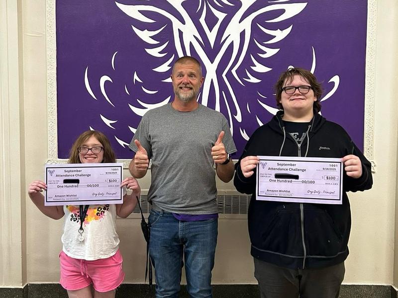 Two students holding attendance challenge checks with a smiling man.
