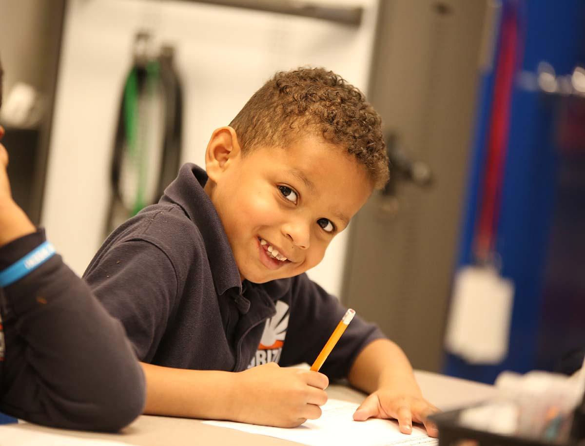 Elementary student smiling and writing in class.