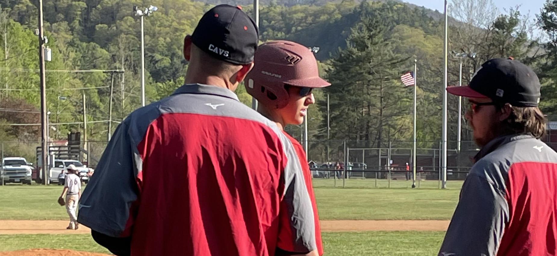 Two baseball coaches talk to a player on a field.