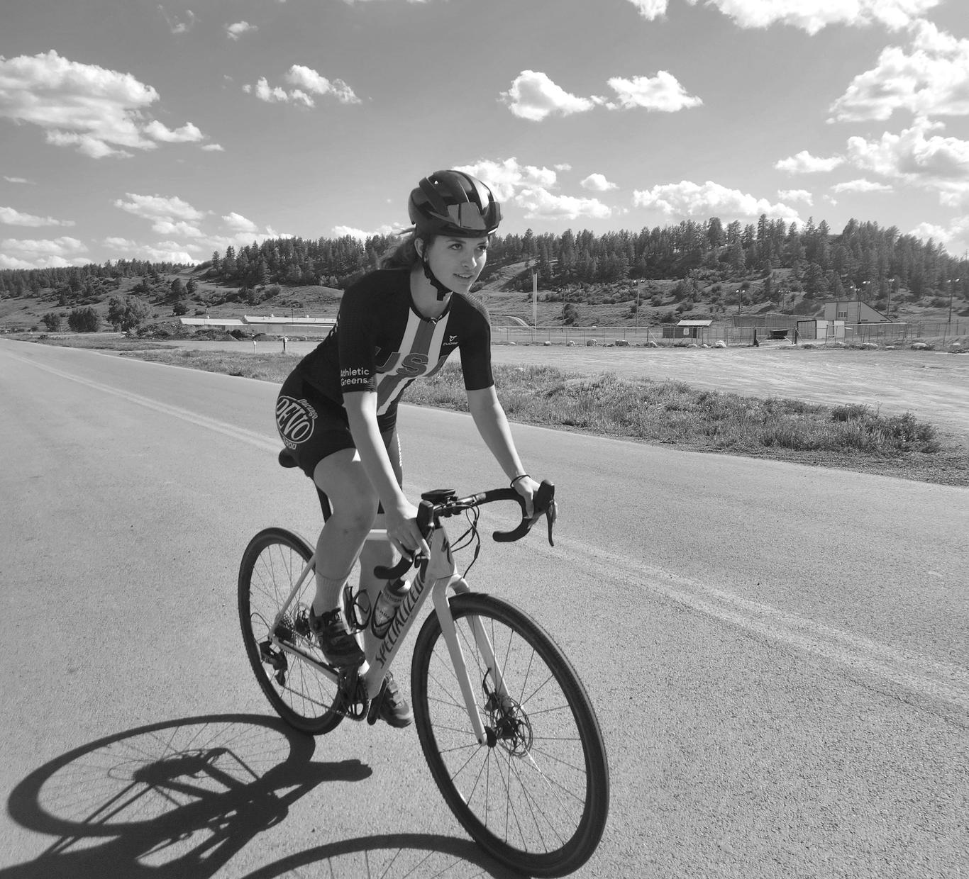 Athlete riding a bicycle on a rural road under a blue sky.