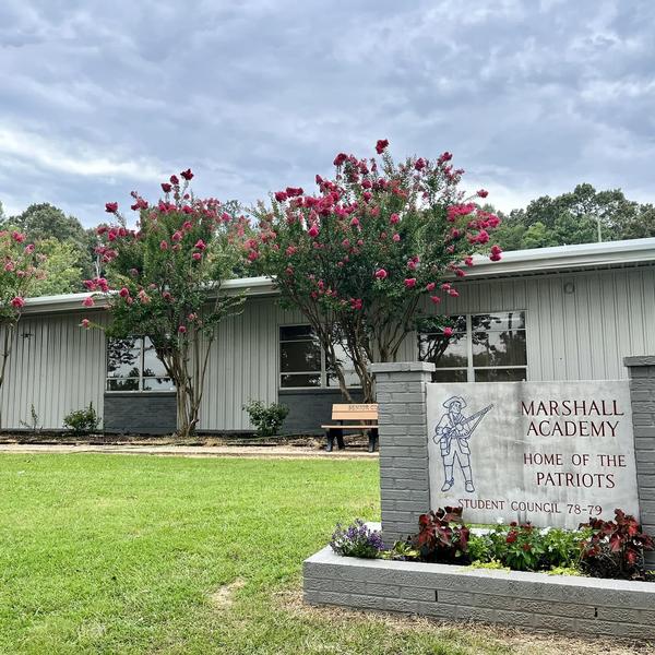 Gray building with flower trees and a sign for Marshall Academy.