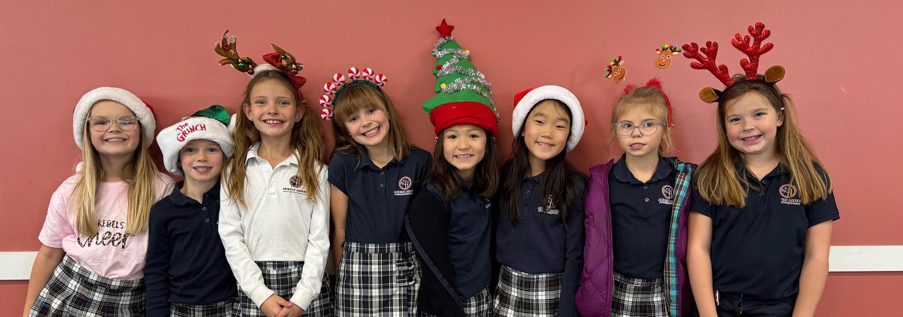 Eight girls in festive hats and school uniforms smiling together in a holiday setting.