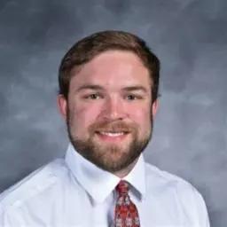 Young man with a beard in a dress shirt and tie against a gray backdrop.