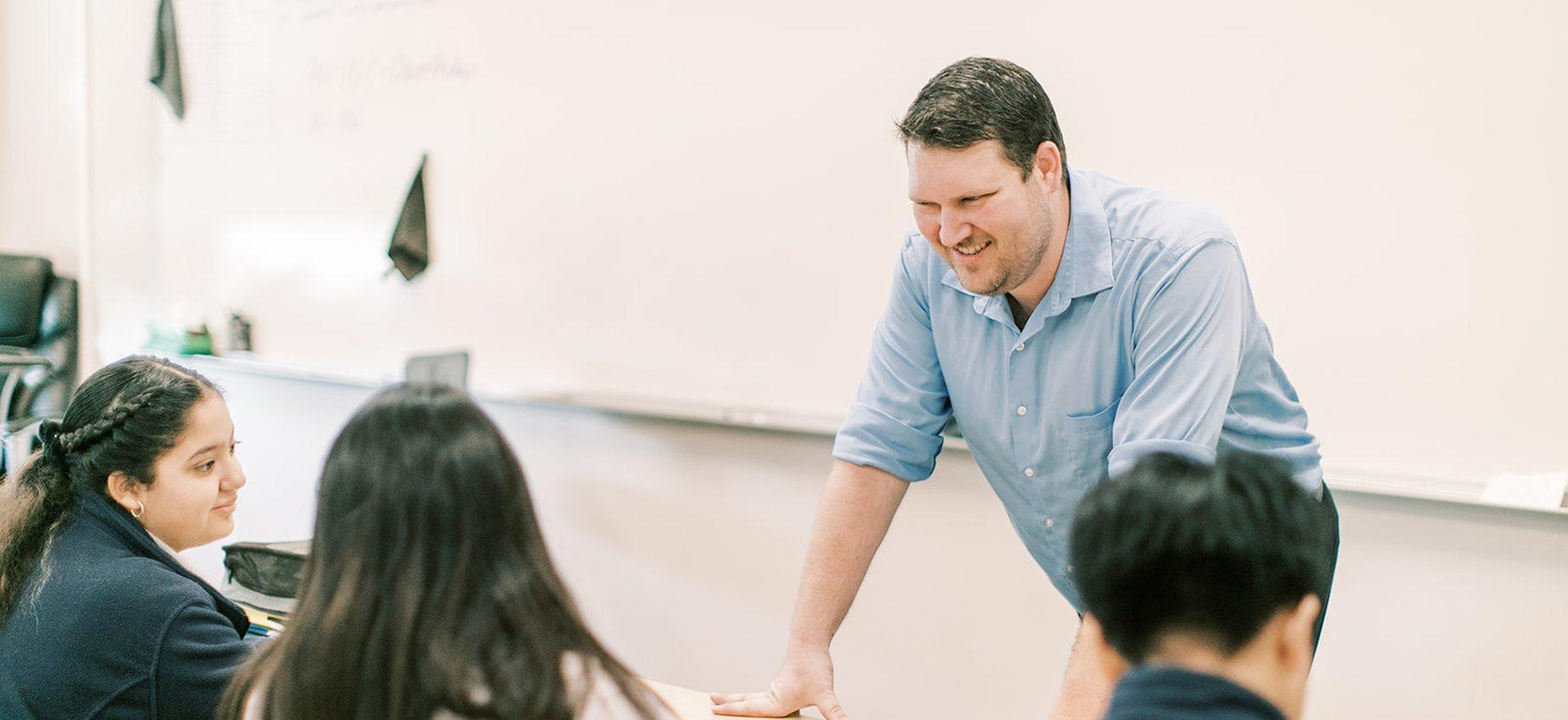 A smiling teacher helps students at their desks